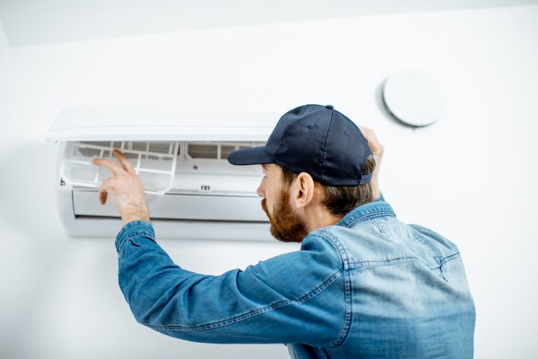 Repairman in blue workwear serving the air conditioner changing filter on the white wall background